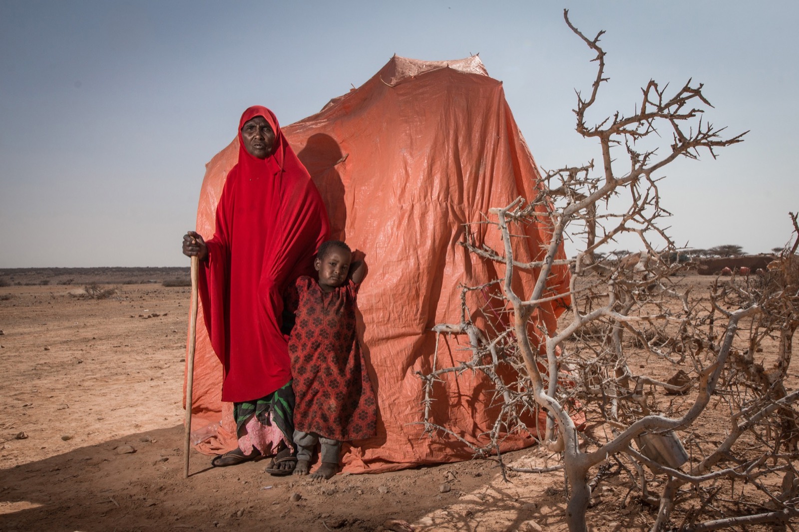 BBC, photo 06. Grandmother Amina stands with her daughter in front of a makeshift shelter in an informal settlement outside Yogoori.